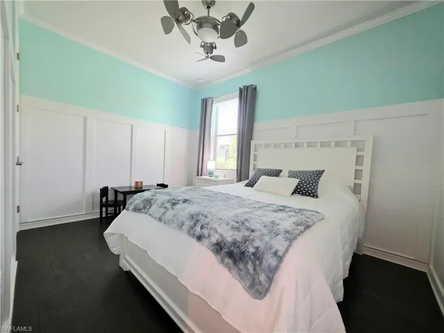 Bedroom with a decorative wall, ornamental molding, a wainscoted wall, dark wood finished floors, and a ceiling fan
