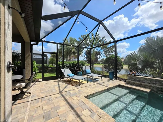View of patio / terrace featuring a sunroom, a hot tub, glass enclosure, and a water view