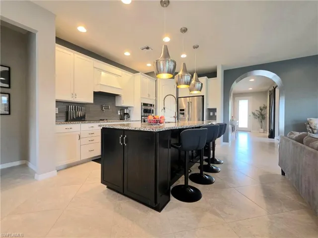 Two tone kitchen featuring arched walkways, a breakfast bar area, stainless steel appliances, light stone counters, and hanging light fixtures