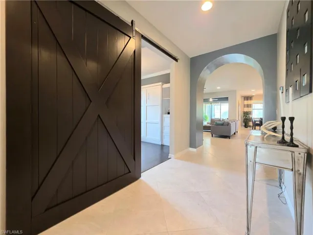 Corridor with arched walkways, a barn door, recessed lighting, crown molding, and light tile patterned flooring