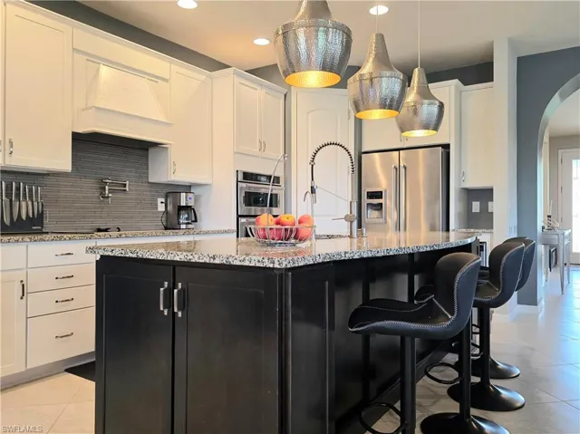 Dual tone kitchen featuring arched walkways, stainless steel appliances, a breakfast bar, decorative light fixtures, and decorative backsplash