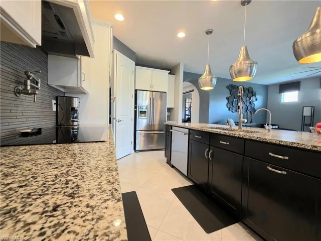 Dual tone kitchen with extractor fan, stainless steel appliances, light stone counters, arched walkways, and hanging light fixtures
