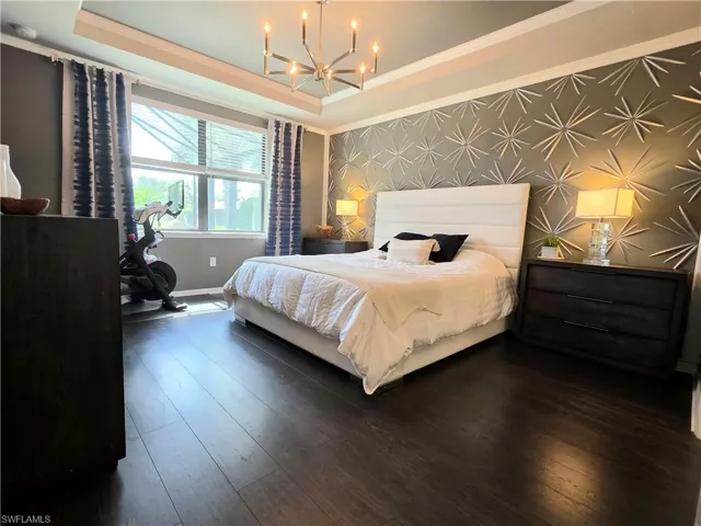 Bedroom featuring an accent wall, a raised ceiling, wallpapered walls, hardwood / wood-style flooring, and a chandelier