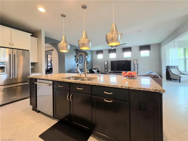 Kitchen with stainless steel appliances, open floor plan, arched walkways, an island with sink, and light stone countertops