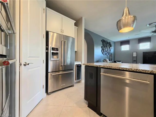 Kitchen featuring stainless steel appliances, arched walkways, white cabinets, ceiling fan, and pendant lighting