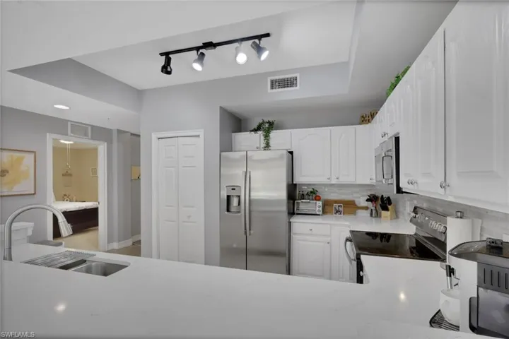 Kitchen featuring stainless steel appliances, light stone counters, tasteful backsplash, white cabinetry, and rail lighting