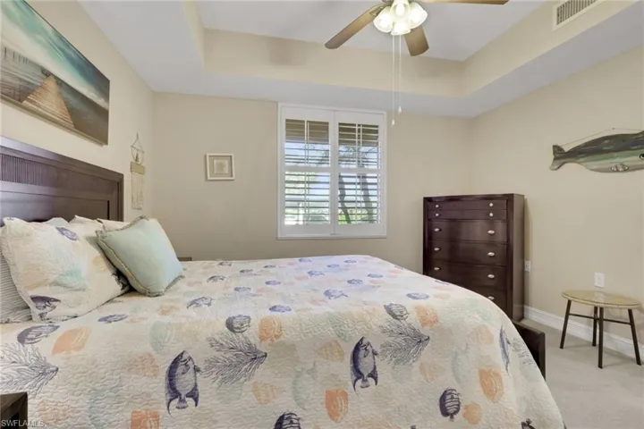 Bedroom featuring a raised ceiling, light colored carpet, and ceiling fan