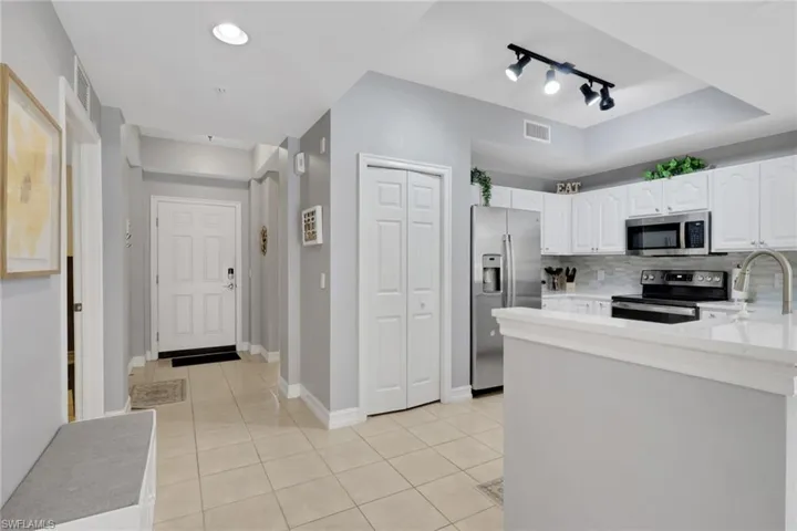 Kitchen with stainless steel appliances, white cabinets, rail lighting, and light tile patterned flooring