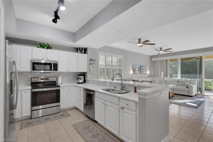 Kitchen featuring light tile patterned flooring, white cabinets, stainless steel appliances, and a peninsula