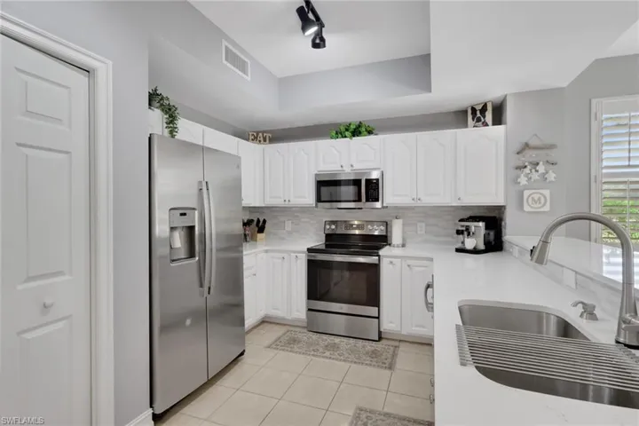 Kitchen with appliances with stainless steel finishes, white cabinets, light stone counters, a raised ceiling, and light tile patterned floors