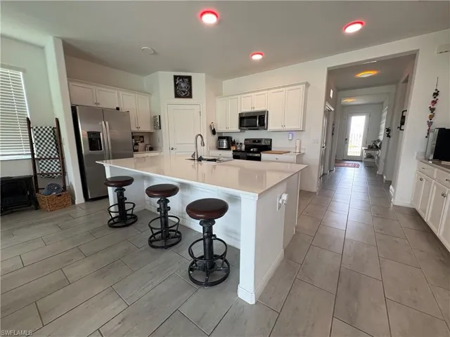 Spacious kitchen featuring an expansive central island with countertop seating, white shaker cabinetry, stainless steel appliances, and large format tile flooring