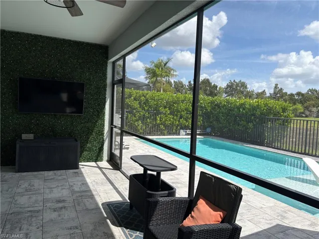 Screened lanai featuring a ceiling fan, a faux-foliage accent wall, and porcelain tile flooring