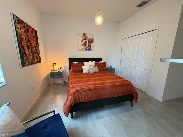 Bedroom featuring light-toned plank tile flooring, a built-in closet with bi-fold doors, a single pendant light fixture, and white baseboards