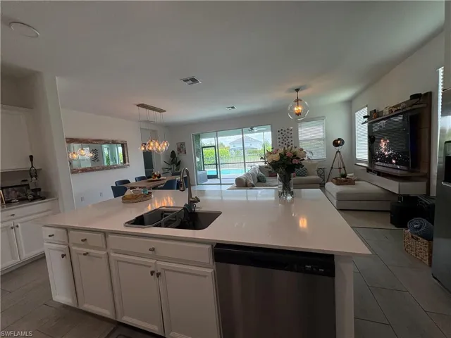 Spacious open-concept interior featuring a kitchen island with an undermount sink, white cabinetry, and stainless steel dishwasher