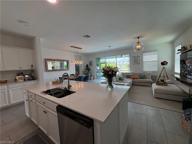 Open-concept kitchen and living area featuring a large center island with an undermount sink, white cabinetry, stainless steel dishwasher, and tile flooring