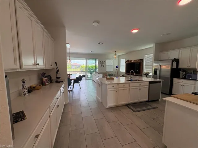 Kitchen featuring white shaker-style cabinetry, a large center island with integrated sink, stainless steel appliances, and a light-toned countertop
