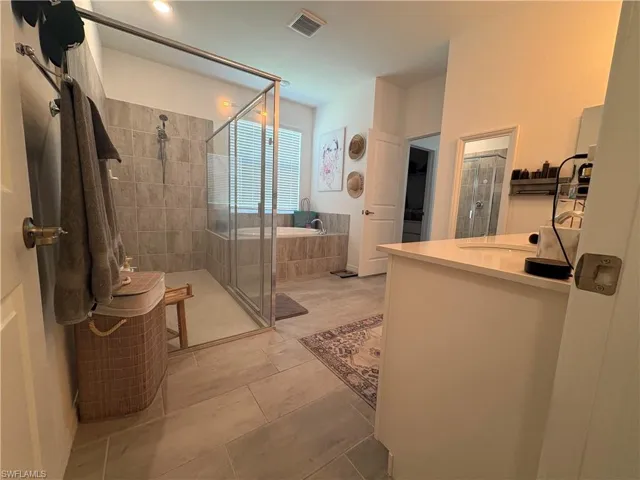 Bathroom featuring a glass-enclosed shower, a built-in soaking tub, a single vanity with a solid surface countertop, and large format tile flooring