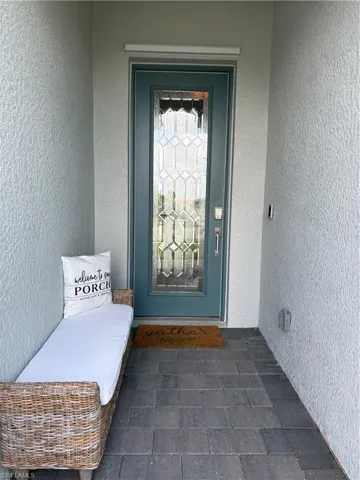 Entryway featuring a decorative glass panel door with sidelights, textured exterior walls, and dark gray paver flooring