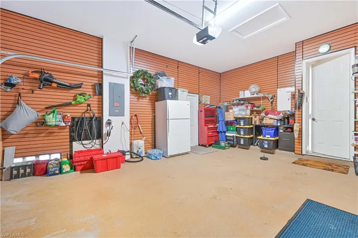 Garage with freestanding refrigerator, electric panel, wood walls, and a garage door opener