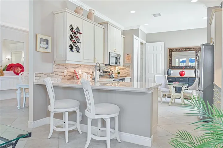 Kitchen featuring ornamental molding, light tile patterned floors, a kitchen breakfast bar, backsplash, and a peninsula