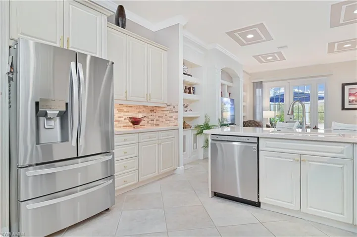 Kitchen with stainless steel appliances, crown molding, white cabinetry, light stone counters, and light tile patterned floors