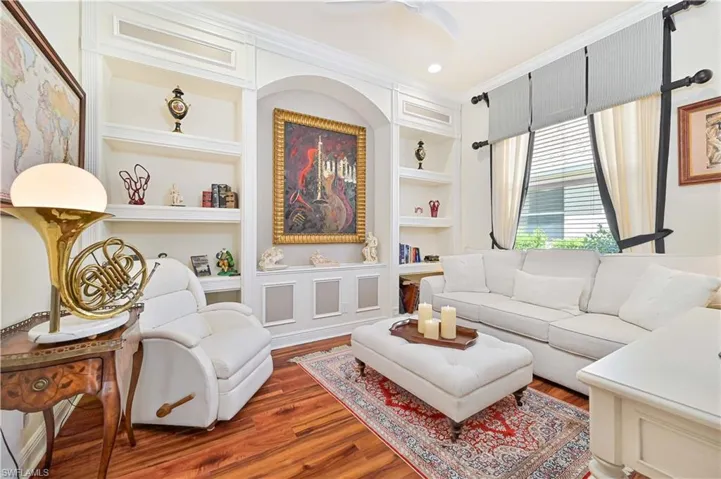 Living area with built in features, crown molding, wood finished floors, and a ceiling fan