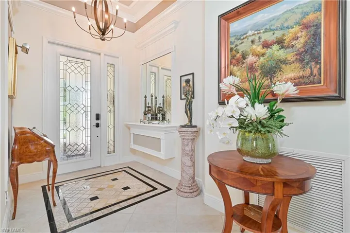 Entryway featuring inlaid floor details, light tile patterned floors, crown molding, and a chandelier