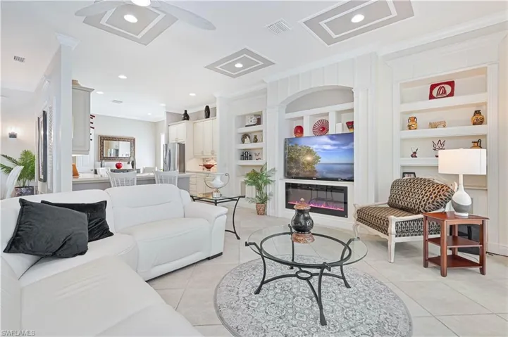 Living area featuring ornamental molding, a ceiling fan, a glass covered fireplace, light tile patterned floors, and built in shelves