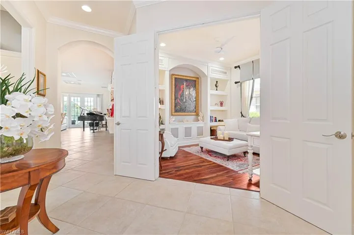 Corridor with built in features, light tile patterned floors, healthy amount of natural light, crown molding, and arched walkways