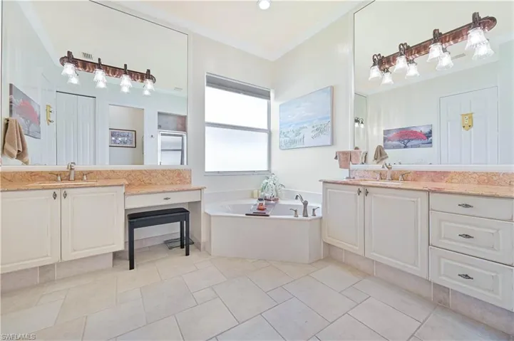 Bathroom featuring a garden tub, two vanities, crown molding, light tile patterned floors, and a closet