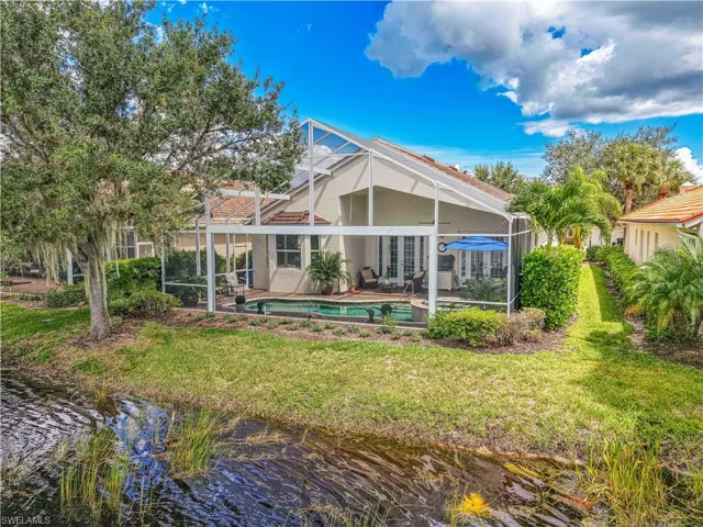 Rear view of property featuring an outdoor pool, a sunroom, a lanai, a yard, and a water view