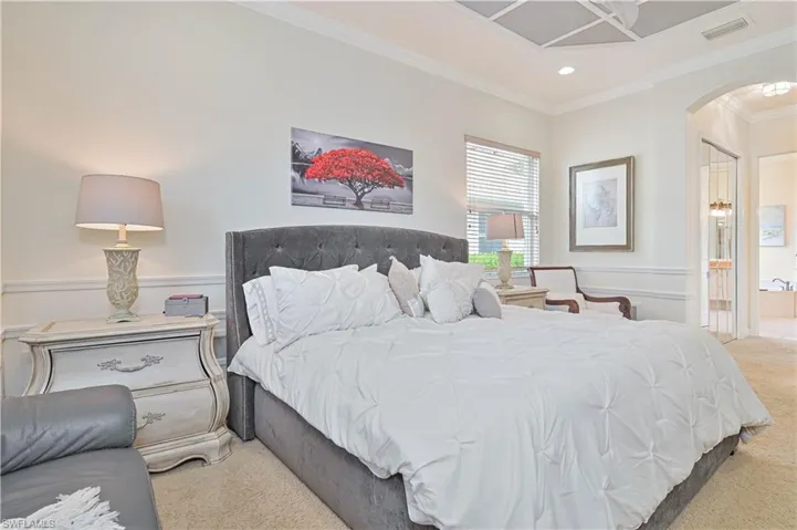 Bedroom with ornamental molding, arched walkways, light colored carpet, connected bathroom, and wainscoting
