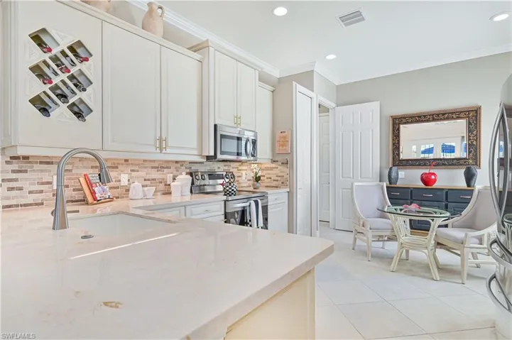 Kitchen with appliances with stainless steel finishes, backsplash, light stone counters, crown molding, and light tile patterned flooring