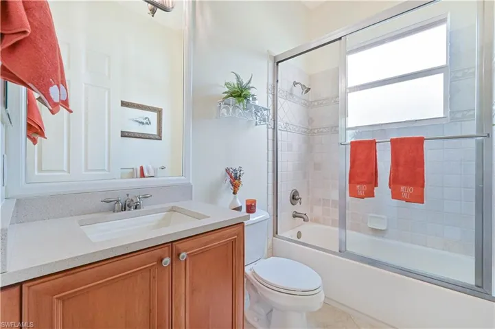Bathroom featuring bath / shower combo with glass door, vanity, and light tile patterned flooring
