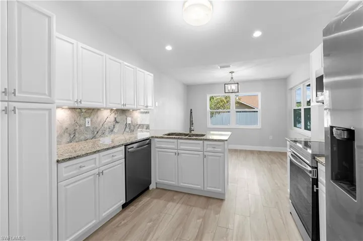 Kitchen with sink, appliances with stainless steel finishes, white cabinetry, tasteful backsplash, and kitchen peninsula