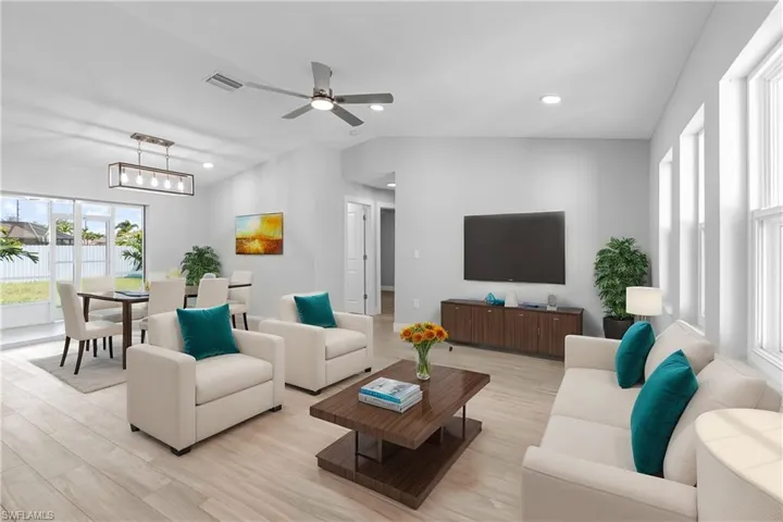 Living room with vaulted ceiling, ceiling fan with notable chandelier, and light hardwood / wood-style floors