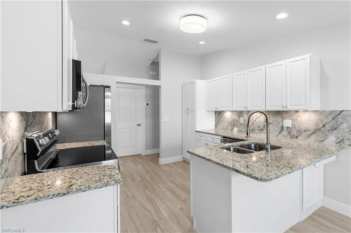 Kitchen featuring white cabinetry, sink, kitchen peninsula, stainless steel appliances, and light stone countertops