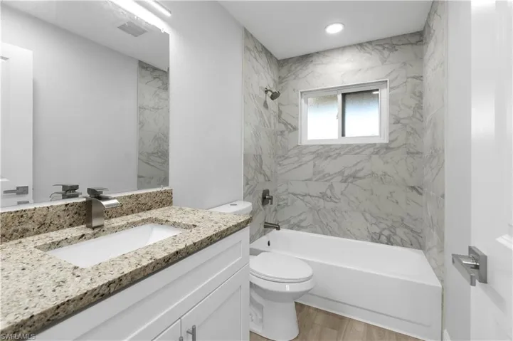 Full bathroom featuring vanity, hardwood / wood-style floors, tiled shower / bath combo, and toilet