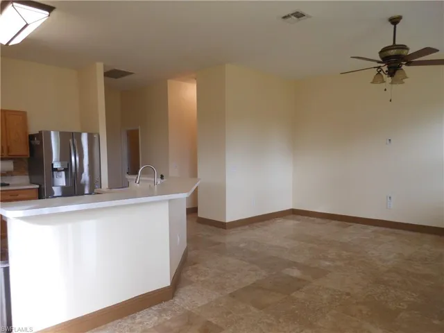 Kitchen with stainless steel fridge, light countertops, a ceiling fan, a kitchen island with sink, and brown cabinets