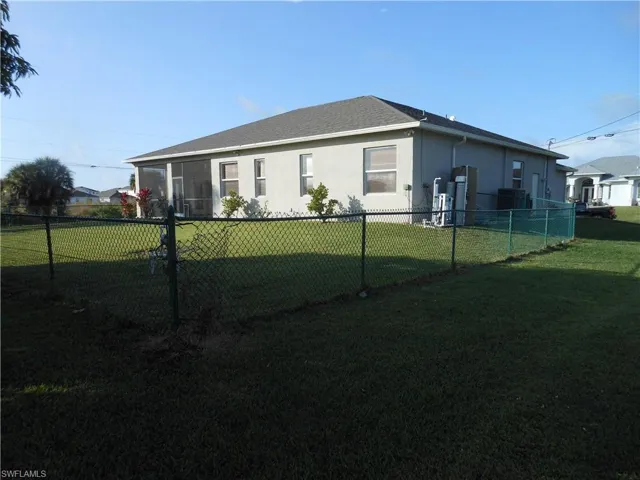 Rear view of property with a sunroom, stucco siding, a fenced backyard, and roof with shingles