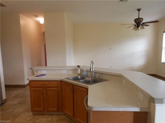 Kitchen featuring brown cabinetry, light countertops, a kitchen island with sink, and a ceiling fan