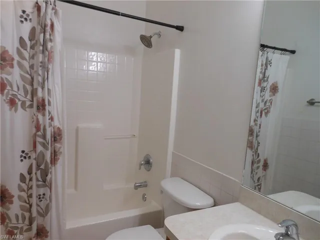 Bathroom with vanity, tile walls, shower / bathtub combination with curtain, and a wainscoted wall