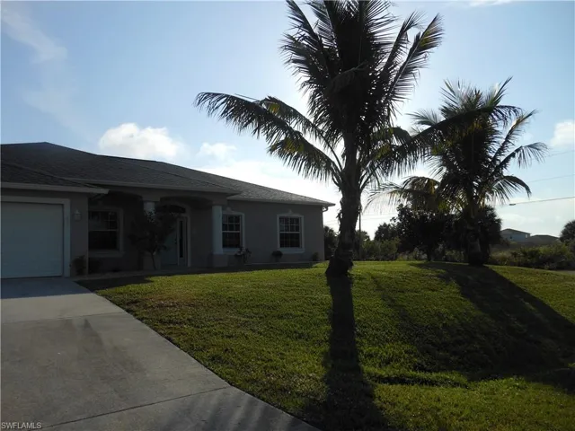 Single story home featuring driveway, a front lawn, an attached garage, and stucco siding