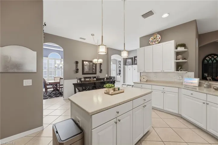 Kitchen featuring an island, white cabinetry, light countertops, subway tile backsplash, and tile flooring