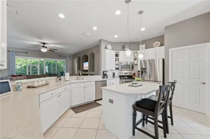 Kitchen featuring white cabinetry, light-toned countertops, a central island with pendant lighting, stainless steel appliances, and tile flooring