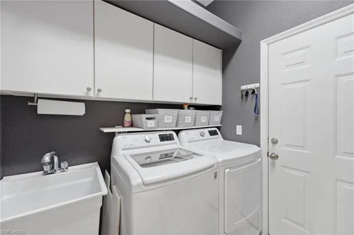Dedicated laundry area featuring a utility sink with chrome faucet, upper white cabinetry, and a white paneled door