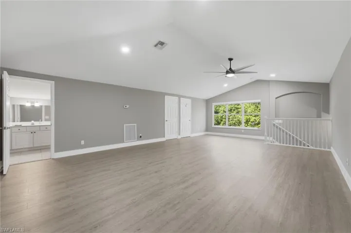 Spacious room featuring vaulted ceilings, recessed lighting, wood-finish flooring, a contemporary ceiling fan, and large windows with exterior foliage