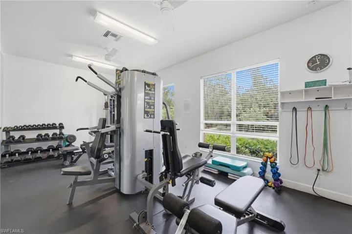 Dedicated fitness space featuring rubber flooring, abundant natural light from large windows, two ceiling fans, and overhead fluorescent lighting