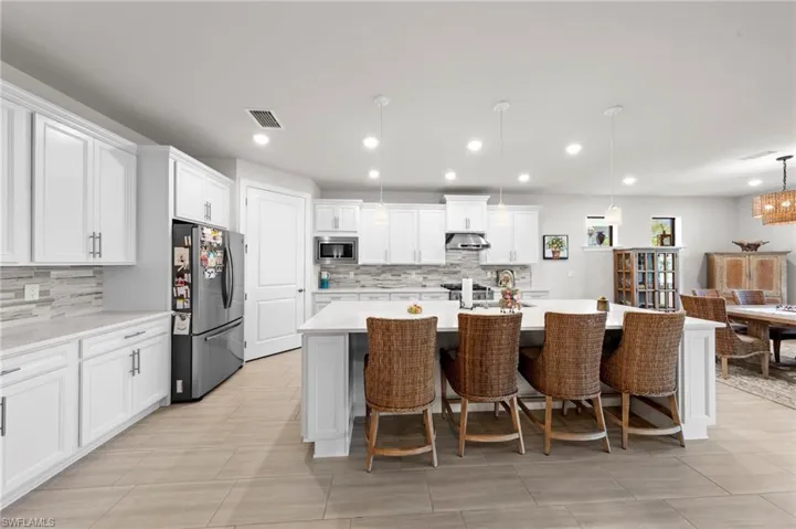 Kitchen with a breakfast bar, white cabinetry, appliances with stainless steel finishes, hanging light fixtures, and a center island with sink