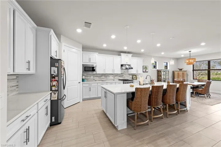 Kitchen with a kitchen bar, hanging light fixtures, a center island with sink, white cabinets, and stainless steel appliances